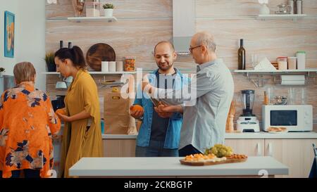 Une grande famille met les provisions dans le réfrigérateur. Un jeune couple venant du shopping apporte un sac en papier avec des provisions, des aliments frais du supermarché à la maison des parents pour préparer un dîner en famille Banque D'Images