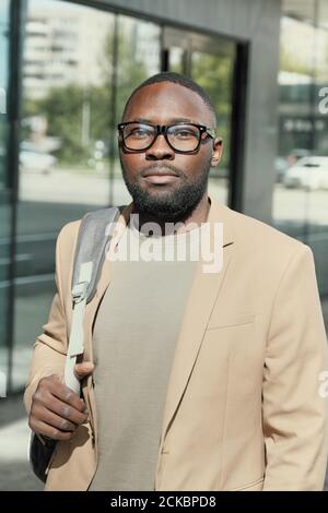Portrait d'un jeune homme africain en lunettes regardant l'appareil photo tout en marchant le long de la rue à l'extérieur Banque D'Images
