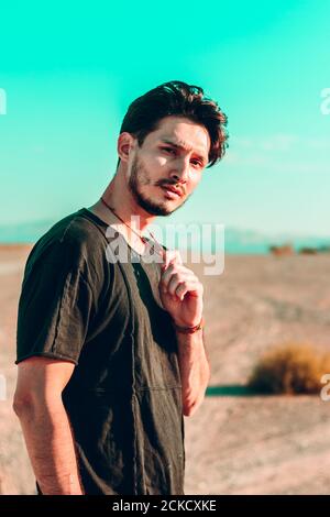 un beau brunette homme dans un désert tenant son collier d'une main et en regardant directement la caméra Banque D'Images