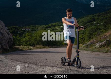 Jeune homme à bord d'un scooter électrique sur la chaîne de montagnes. Concept de transport écologique Banque D'Images