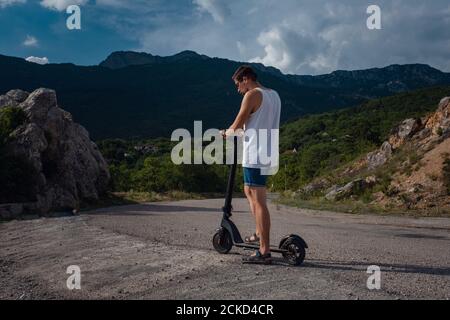 Jeune homme à bord d'un scooter électrique sur la chaîne de montagnes. Concept de transport écologique Banque D'Images