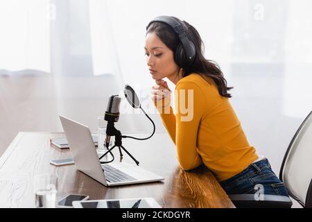 une radio asiatique bien pensée dans un casque sans fil qui touche le menton assis sur le lieu de travail en studio Banque D'Images