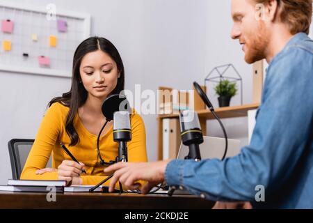 objectif sélectif de la jeune chaîne de télévision asiatique tenant le stylo pendant l'interview avec redhead man Banque D'Images