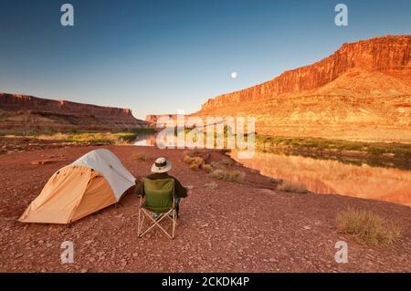 Campeur au camp de Labirynth dans le canyon de Labirynth avec lune au-dessus de Green River, lever du soleil, région de White Rim Road, Parc national de Canyonlands, Utah USA Banque D'Images