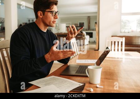 Homme d'affaires travaillant à la maison parlant sur un téléphone à haut-parleur. Homme assis à une table avec un ordinateur portable pour passer un appel téléphonique. Banque D'Images