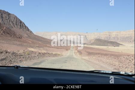 Vue sur la campagne de montagne aride dans Timna Park situé dans le désert du Negev en Israël. La vue est de la fenêtre avant de la voiture qui passe devant une route asphaltée sale. Banque D'Images