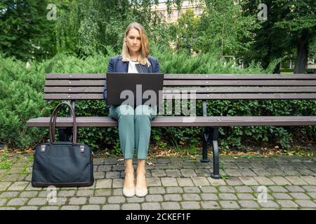 jeune femme d'affaires assise sur le banc dans le parc de la ville et travaillant sur ordinateur portable. travail indépendant de bureau extérieur Banque D'Images