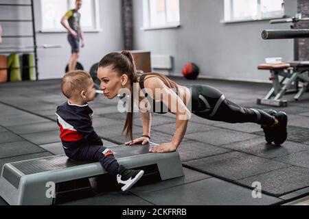 Jeune femme en forme faisant des push-up et embrassant son petit fils Banque D'Images