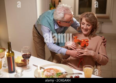 Homme âgé donnant des fleurs à sa femme et la félicitant avec leur anniversaire pendant le dîner Banque D'Images
