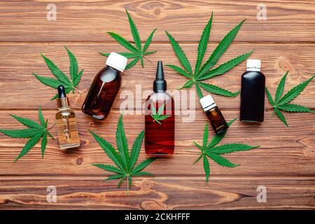 Cannabis liquides médicaux et produits cosmétiques. Bouteilles d'huile de chanvre cbd et de médicaments avec des feuilles de marijuana et de mauvaises herbes sur fond de bois brun Banque D'Images