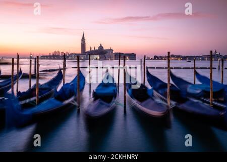 Gondoles amarrées dans la Laguna Veneta avec le Bazilika San Giorgio Maggiore en arrière-plan pendant le lever du soleil à Venise, en Italie Banque D'Images