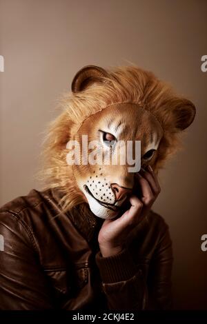 portrait d'un homme portant un masque de lion soutenant sa tête dans sa main, sur fond beige, avec un traitement rétro Banque D'Images