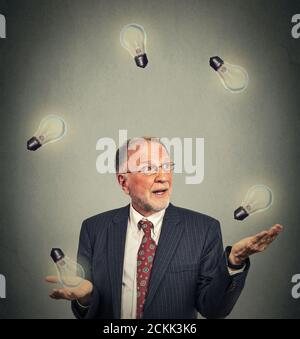 Portrait heureux homme d'affaires senior cadre en costume jonglant jouant avec ampoules isolées sur fond gris de mur de bureau Banque D'Images