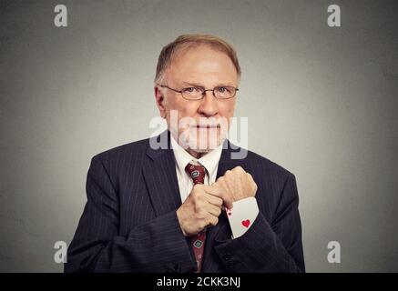 Gros plan portrait homme senior transaction Maker en tirant un caché carte ace de la housse de costume isolée sur le gris arrière-plan de la paroi Banque D'Images