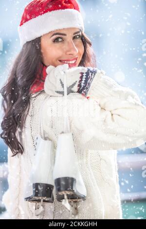 Fille en chapeau de Noël et chandail blanc tient des patins à glace dans sa main à travers son épaule. Banque D'Images