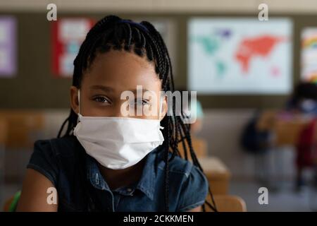 Portrait d'une fille portant un masque de visage assis dans le classe à l'école Banque D'Images
