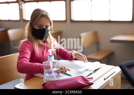 Fille portant un masque facial assis sur son bureau à l'école Banque D'Images