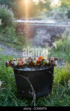 Kebab végétarien aux légumes sur brochettes cuisant sur barbecue fumé par jolie piste de remorquage côté canal à côté de narrowboat en été à crépuscule Banque D'Images