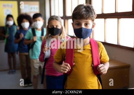 Groupe d'enfants portant des masques avec des sacs debout dans une file d'attente à l'école Banque D'Images