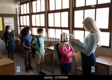 Enseignante mesurant la température d'une fille en classe à école Banque D'Images