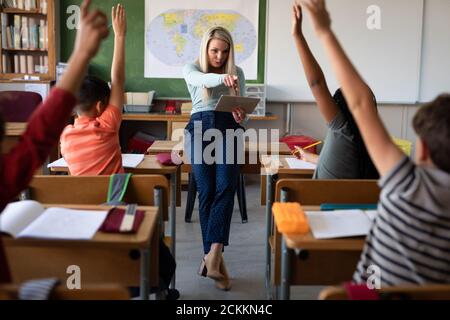 Une enseignante pointant vers des enfants levant les mains en classe à l'école Banque D'Images