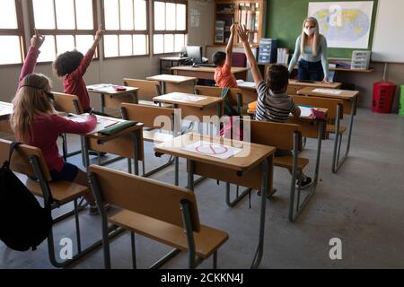 Groupe d'enfants portant un masque facial levant les mains la classe Banque D'Images