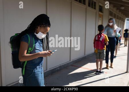 Fille portant un masque facial utilisant un smartphone à l'école Banque D'Images