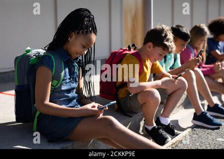 Groupe d'enfants utilisant un smartphone tout en étant assis ensemble Banque D'Images