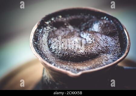 Café naturel avec mousse épaisse, brassé dans une cève de cuivre de la manière classique, sur un fond de bois, photo macro. Banque D'Images