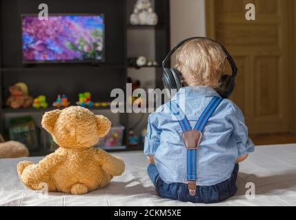 Un joli petit garçon avec un casque et son ours en peluche Téléviseur assis sur un canapé dans le salon à accueil Banque D'Images