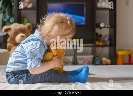 Un joli petit garçon et son ours en peluche regardant la télé s'asseoir sur un canapé dans le salon à la maison Banque D'Images