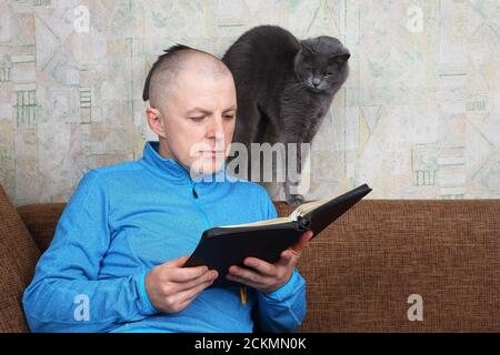 homme assis sur un canapé et lisant un livre de la Bible Banque D'Images