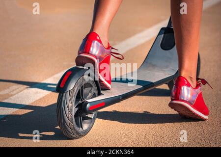 Jeune femme avec de belles jambes dans des sneakers rouges debout avec scooter électrique Banque D'Images