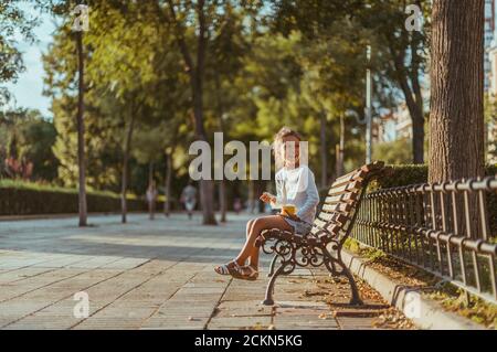 Un enfant mange de la crème glacée sur un banc de parc Banque D'Images