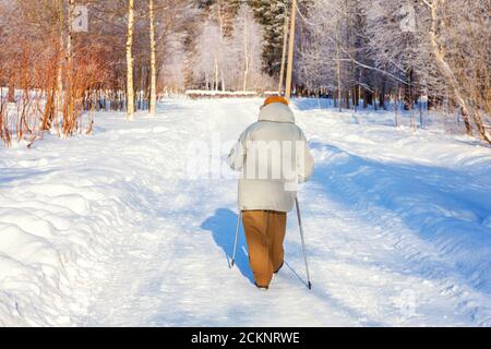 Femme adulte dans les vêtements de sport d'hiver avec bâtons pour la marche nordique sur l'hiver paysage ville parc arrière, vue arrière. Femme mature faisant de l'exercice à l'extérieur. Hiver soprt concept de mode de vie sain. Banque D'Images