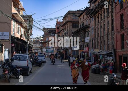 Bhaktapur, Katmandou, Népal - 23 décembre 2019 : des personnes non identifiées se promène dans la rue, des motos et des voitures sont garées sur le côté entre les bâtiments Banque D'Images