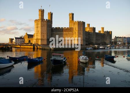 Spectaculaire château de Caernarfon, pays de Galles debout fier de montrer son reflet dans les eaux environnantes avec de petits bateaux en fin de soirée d'été Banque D'Images