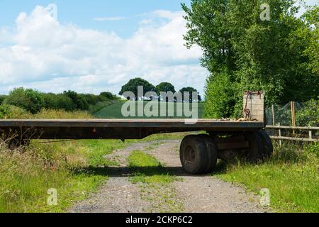 gros plan d'une grande remorque de transport en bois avec roues arrière sur la voie de campagne à l'extérieur de la ferme avec champs et bleu nuageux ciel Banque D'Images