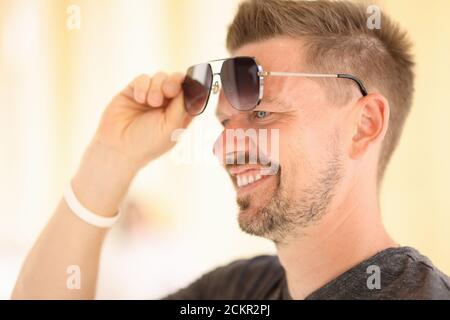 Le beau homme lève les lunettes avec sa main vers le haut de ses yeux. Banque D'Images