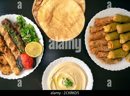 Célèbre cuisine arabe traditionnelle, turque, israélienne. Poulet grillé, kofta kebab, mahshi, choux, pain pita, tahini sur plaque blanche sur bois sombre Banque D'Images