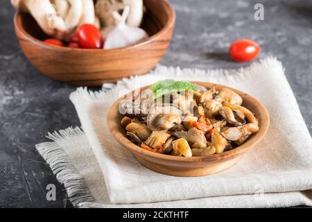 Champignons huîtres frits avec tomates dans une assiette en bois sur fond de béton noir. Vue latérale, gros plan Banque D'Images