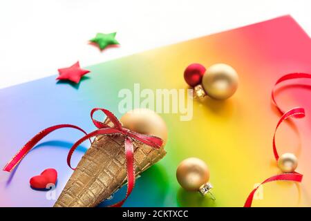 Décorations de Noël en couleurs de drapeau arc-en-ciel de la communauté LGBTQ. Cornet de gaufres à la crème glacée, boules métalliques d'or, étoiles et forme de coeur sur papier arc-en-ciel Banque D'Images