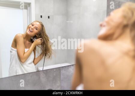 Happy young woman blow drying hair dans salle de bains Banque D'Images