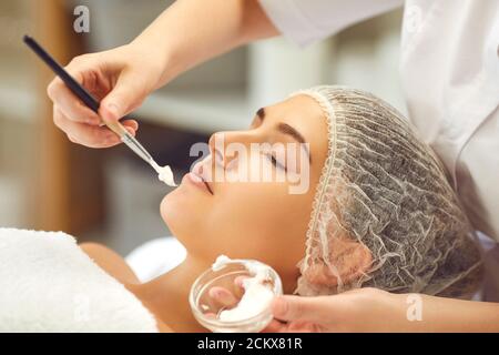 Mains du dermatologue mettant la crème hydratante au visage des femmes pendant soins de la peau dans le salon de spa Banque D'Images