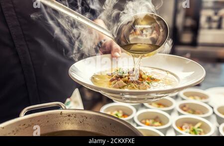 Le chef verse le bouillon dans une soupe de poulet aux nouilles, à la viande et aux légumes Banque D'Images