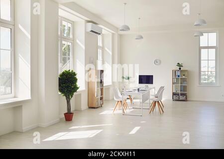 Lieu de travail dans un bureau moderne et lumineux avec de grandes fenêtres, une table blanche et des chaises. Banque D'Images