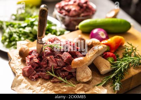 Viande de cerf en tranches préparée pour ragoût de champignons de la forêt de gibier herbes, légumes et couteau Banque D'Images