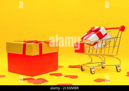 boîte cadeau dans le panier et grande boîte cadeau sur fond jaune à côté des coeurs rouges, espace de copie. Concept de cadeau, Saint-Valentin, vacances Banque D'Images
