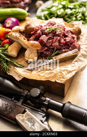 Viande de cerf en tranches préparée pour ragoût de champignons de la forêt de gibier couteau à légumes et fusil de chasse aux herbes Banque D'Images