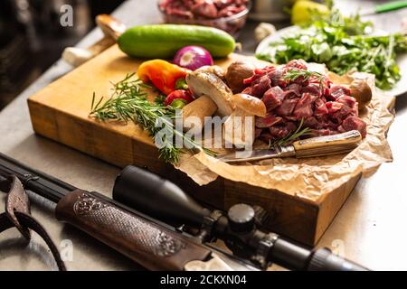 Viande de cerf en tranches préparée pour ragoût de champignons de la forêt de gibier couteau à légumes et fusil de chasse aux herbes Banque D'Images